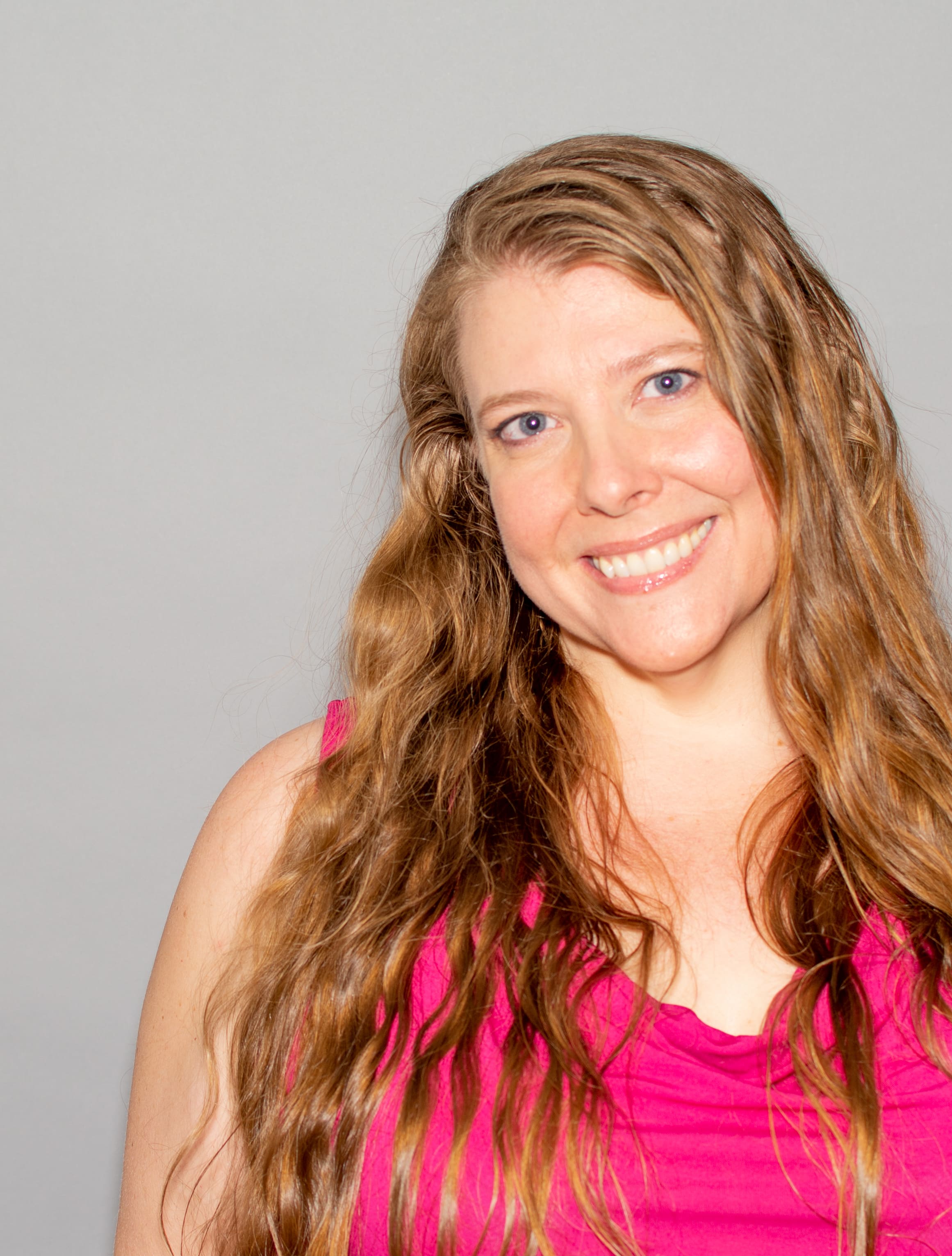 Photo of Jenny in a bright pink blouse with a generous smile, long wavy hair the color of honey, and kind blue eyes.